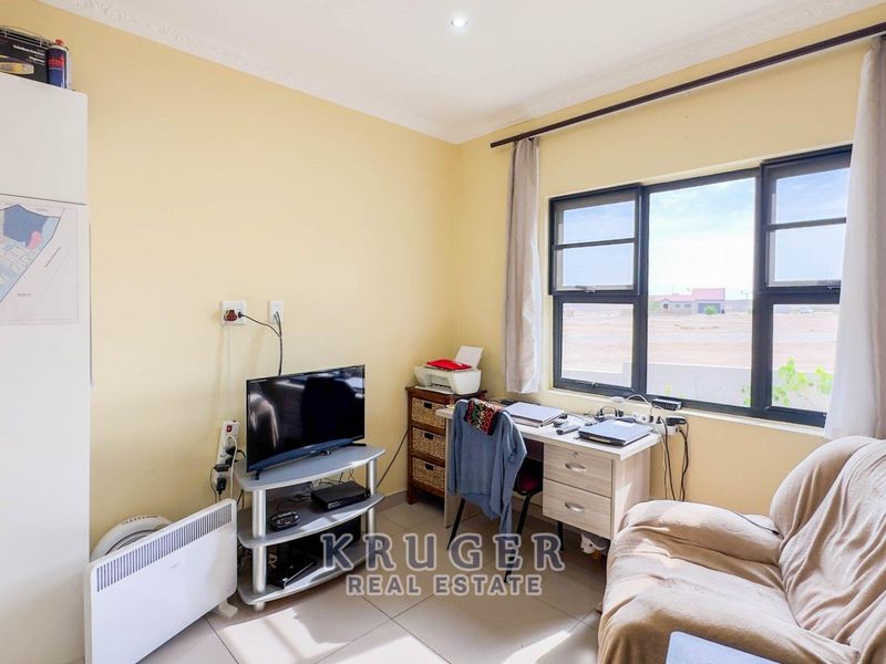 A functional bedroom featuring tiled flooring, a built-in wardrobe, and large aluminium-framed windows providing natural light.