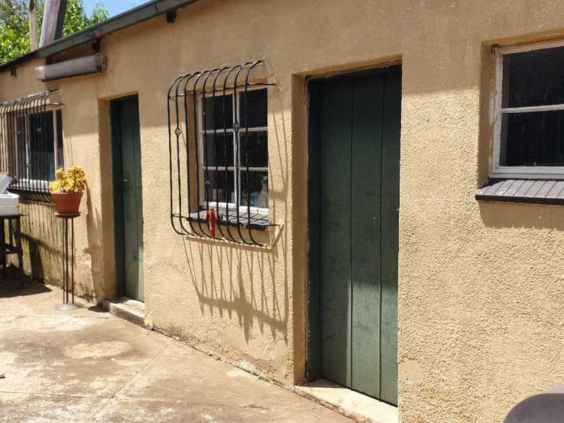 Exterior view of the rear building facade featuring concrete paving, multiple access doors, and windows with security bars.