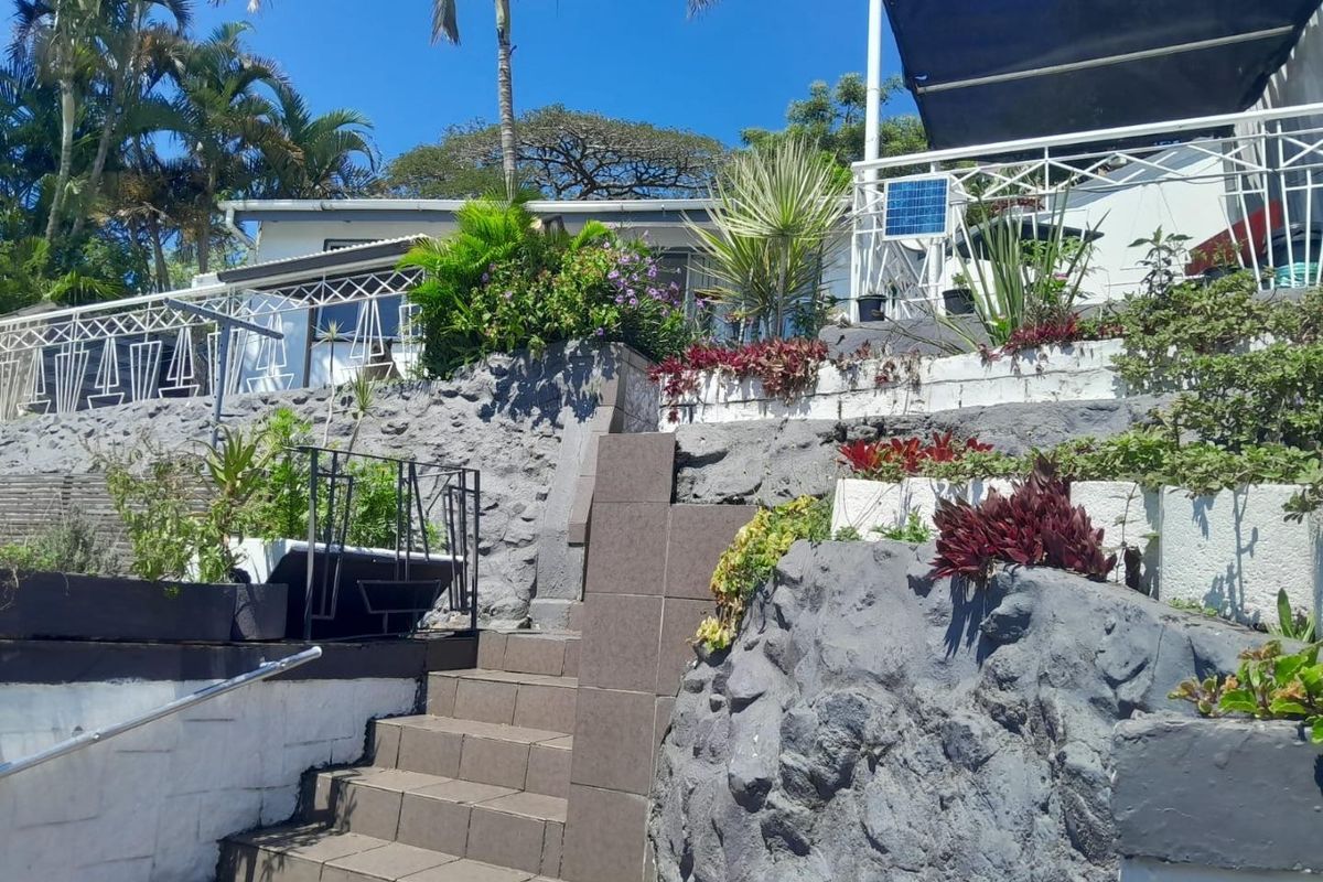 Rear exterior view featuring tiered stone retaining walls, a tiled staircase with metal railings, and a covered patio area.