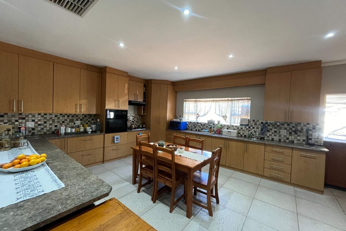 Spacious kitchen featuring light wood cabinetry, tiled flooring, mosaic backsplash, built-in oven, and ample counter space with a central dining area.
