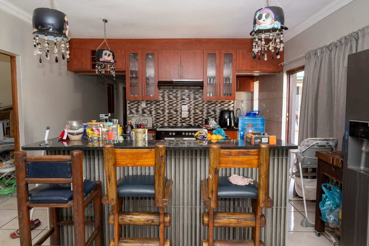 A functional kitchen featuring dark granite countertops, wooden cabinetry, a built-in gas hob with extractor fan, and a breakfast bar island.