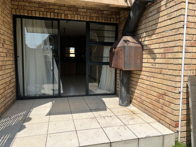 Outdoor patio area featuring tiled flooring, a brick facade, and a built-in braai unit, providing direct access to the interior living space.