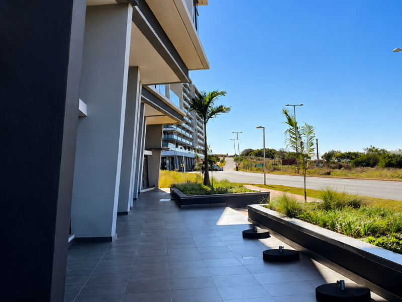 A modern commercial building exterior featuring a clean tiled walkway, contemporary facade design, and integrated landscaping along the street-facing frontage.