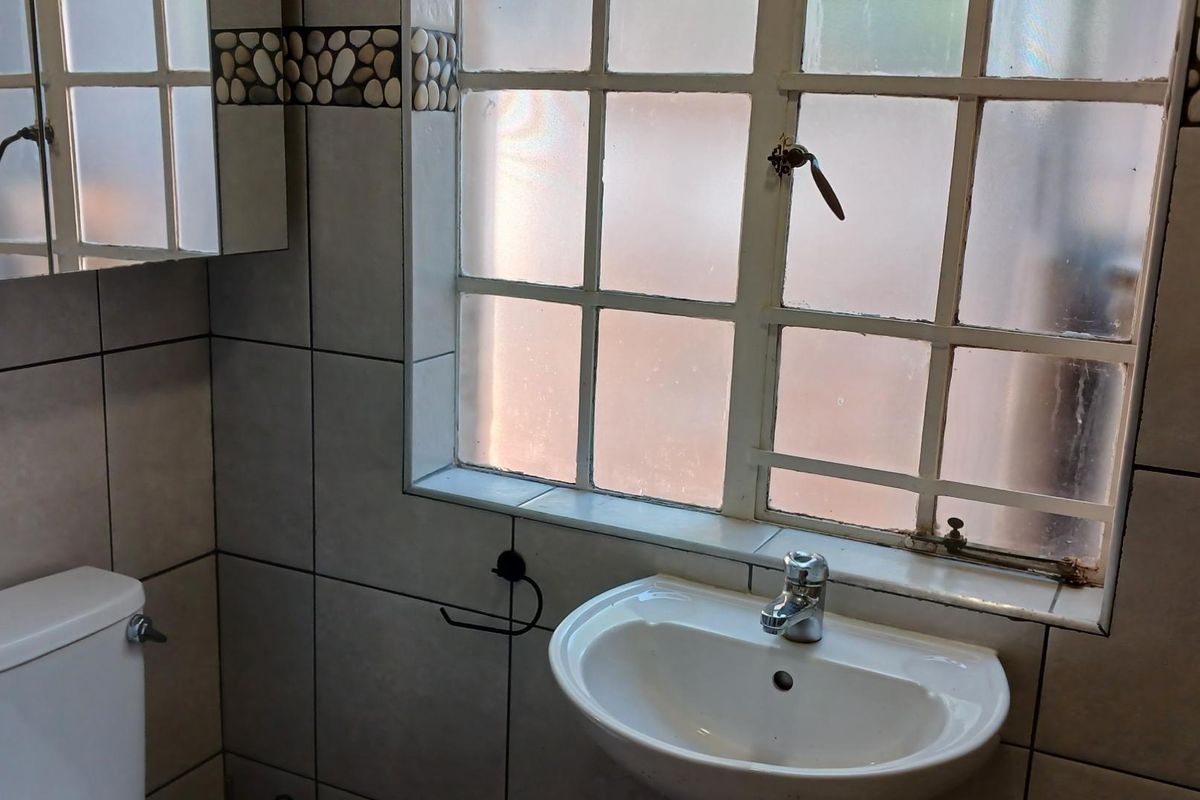 A functional bathroom featuring a pedestal basin, toilet, and tiled walls with a decorative pebble border, illuminated by a frosted window.