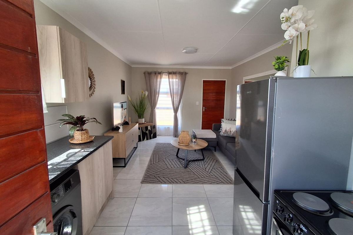 A bright open-plan living area featuring tiled floors, a modern kitchen with stone countertops, and integrated laundry facilities, creating a functional and cohesive space.