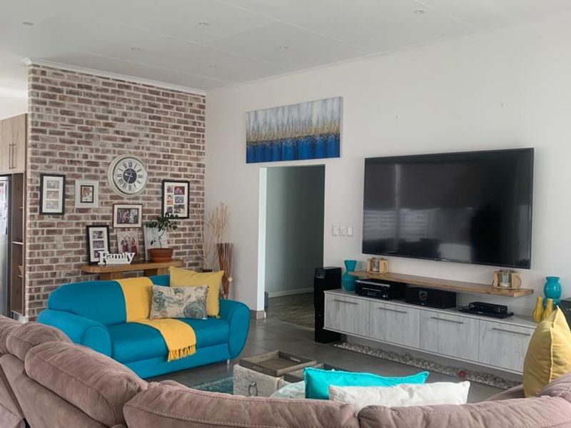 Spacious living room featuring a prominent exposed brick accent wall, neutral tiled flooring, and a modern built-in media console.