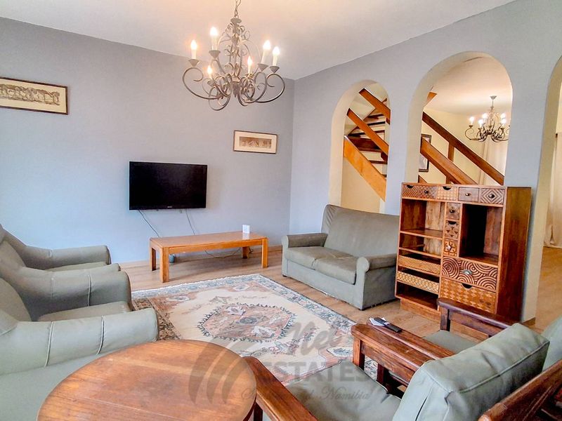 Spacious living room featuring arched architectural details, a wooden staircase, laminate flooring, and a decorative wrought iron chandelier.