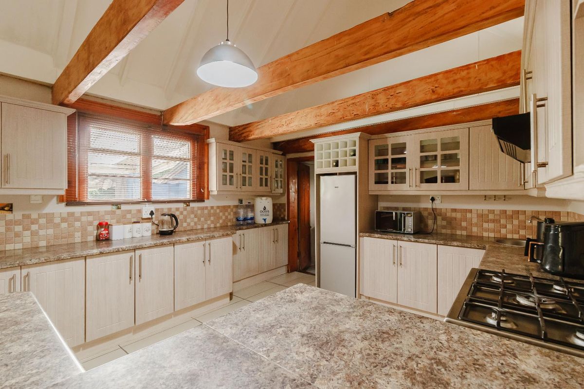 A well-maintained kitchen featuring exposed timber ceiling beams, ample laminate cabinetry, granite-look countertops, and a tiled backsplash with a built-in gas hob.