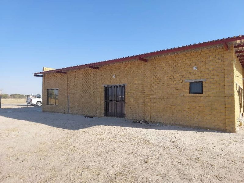 Industrial property exterior featuring exposed brick construction, metal roofing, and secure metal entrance gate on a large open site.