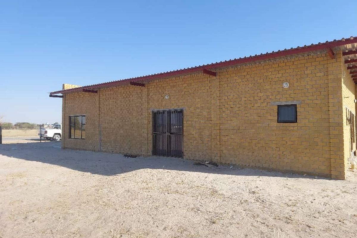 Industrial property exterior featuring exposed brick construction, metal roofing, and secure metal entrance gate on a large open site.