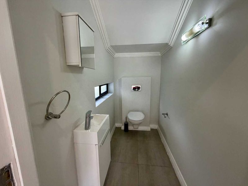 A modern, compact guest bathroom featuring a wall-mounted toilet, vanity basin with mixer tap, and a mirrored medicine cabinet with neutral tiled flooring.