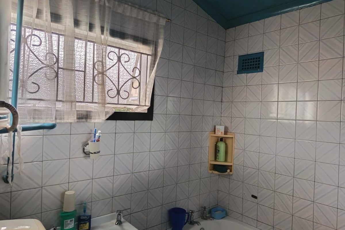 A dated bathroom featuring tiled walls, a standard bathtub, and a washbasin, requiring cosmetic updates to modernize the space.
