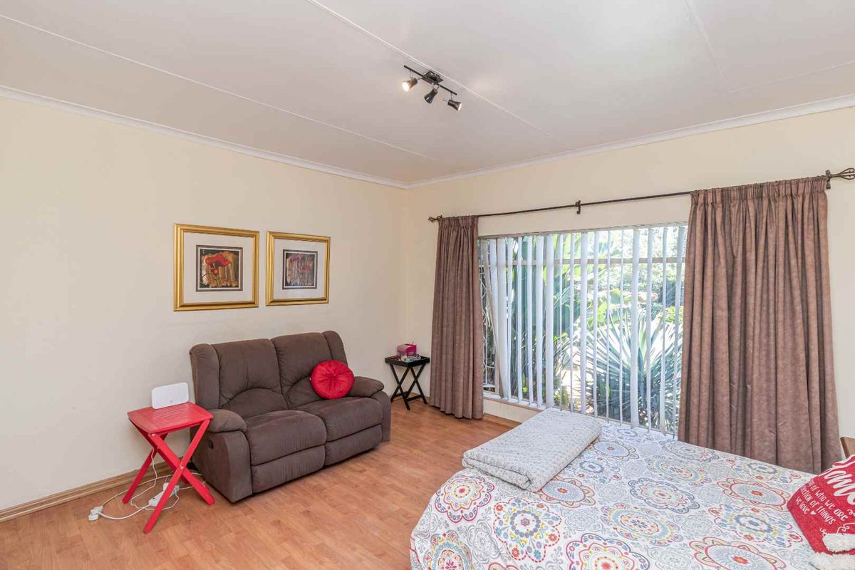 A bedroom featuring laminate flooring, a large window with vertical blinds, and a ceiling-mounted light fixture.