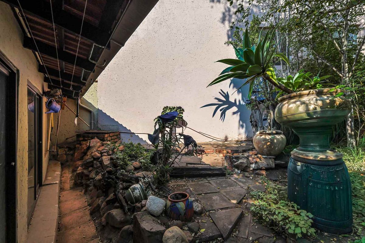 A private rear courtyard featuring paved pathways, rockery garden beds, and a covered patio area adjacent to the main dwelling.