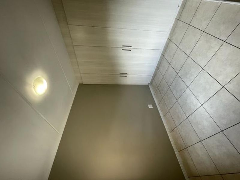 A clean, empty bedroom featuring neutral wall tones, built-in storage cupboards, and durable tiled flooring.