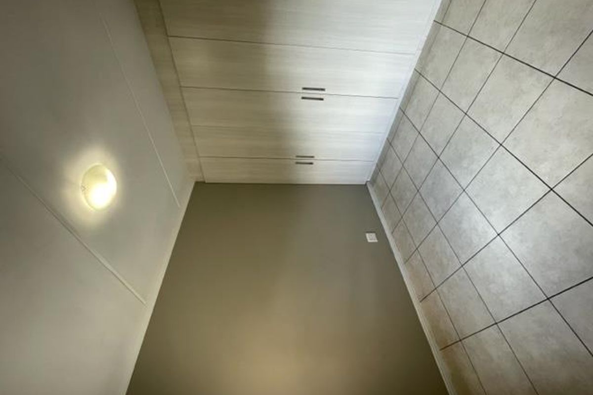 A clean, empty bedroom featuring neutral wall tones, built-in storage cupboards, and durable tiled flooring.