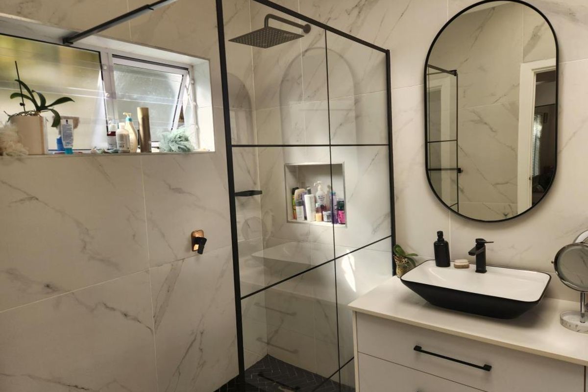 Modern bathroom featuring a walk-in shower with black frame, marble-look wall tiles, a contemporary vanity with vessel sink, and a sleek oval mirror.