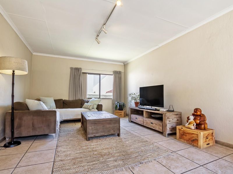 A comfortable living room featuring tiled flooring, neutral walls, and track lighting, providing a functional and well-lit space for relaxation.