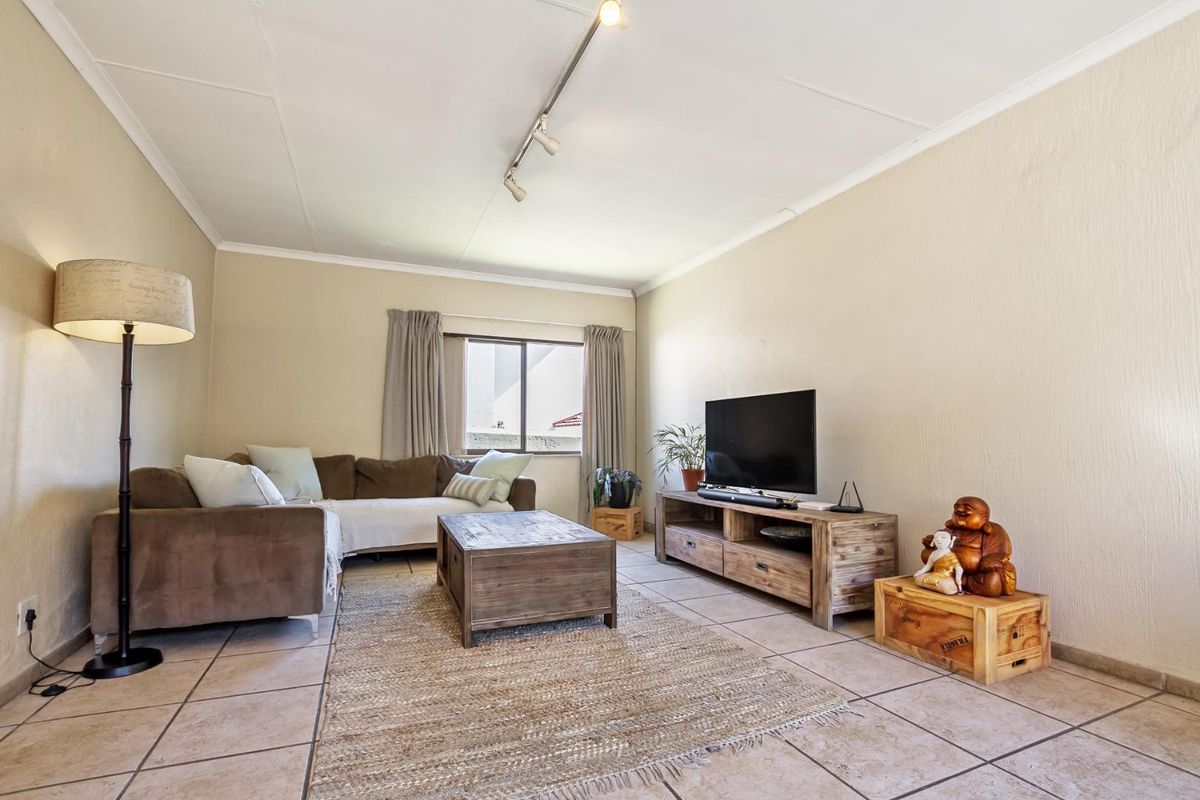 A comfortable living room featuring tiled flooring, neutral walls, and track lighting, providing a functional and well-lit space for relaxation.