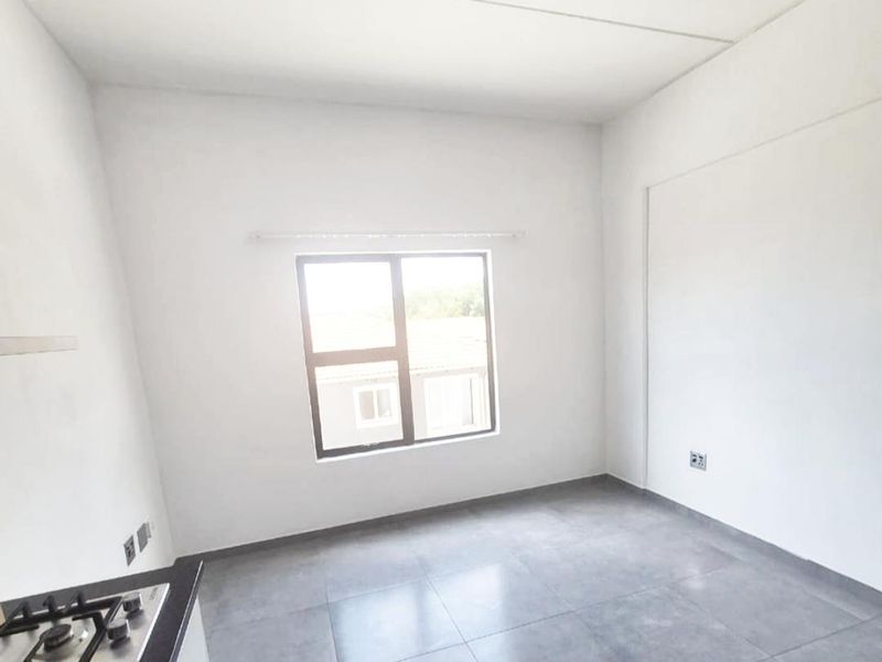 A bright, empty kitchen area featuring modern grey floor tiles, a built-in hob, and a large window providing natural light.