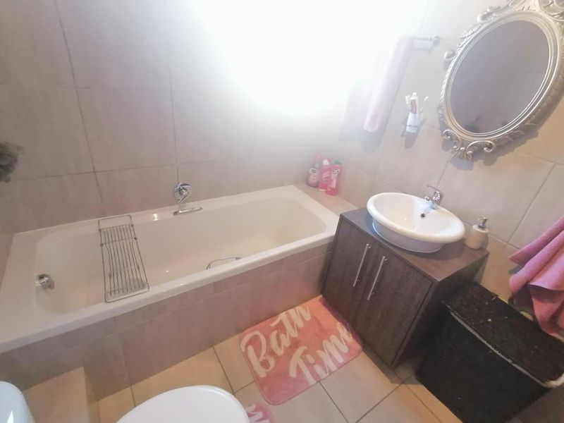 A functional bathroom featuring a built-in bathtub, a modern vessel sink with a vanity cabinet, and neutral wall and floor tiling.