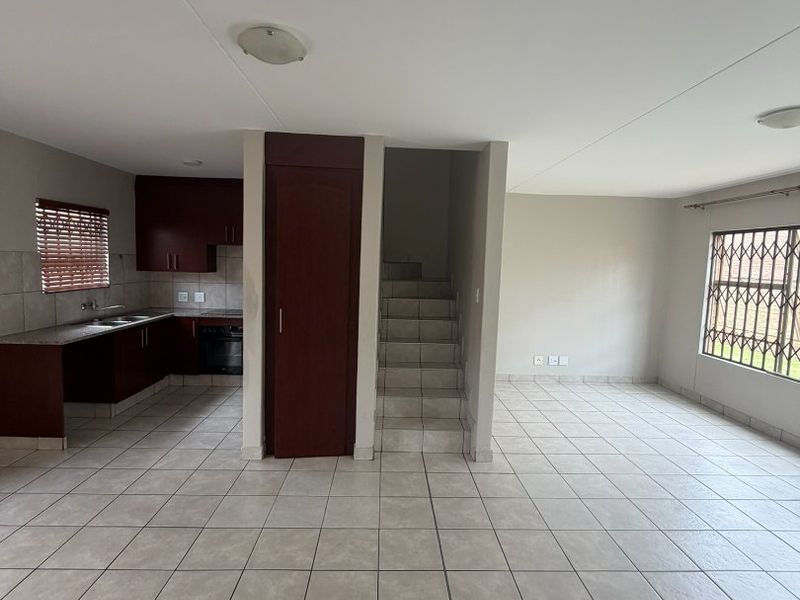 Spacious open-plan living area featuring tiled floors, a functional kitchen with built-in cabinetry, and an internal staircase leading to the upper level.