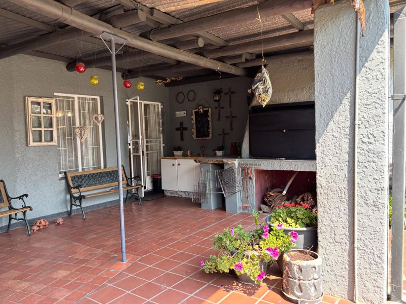 Covered outdoor patio featuring a built-in braai, tiled flooring, and exposed beam ceiling, providing a functional space for outdoor entertaining.