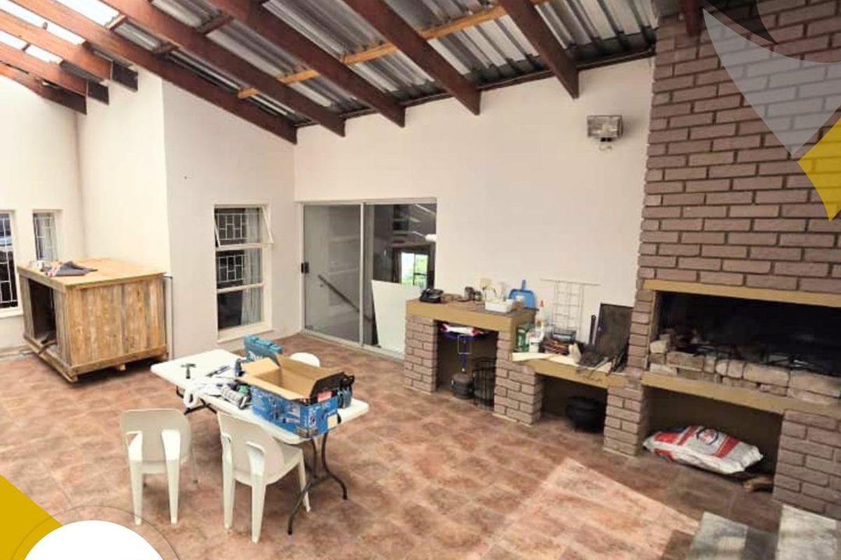 Covered outdoor patio area featuring exposed timber rafters, a built-in brick fireplace, and tiled flooring, providing a versatile space for outdoor entertaining.