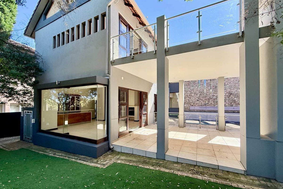 Rear view of the property featuring a covered patio, glass balcony railing, and access to the pool area with landscaped garden.