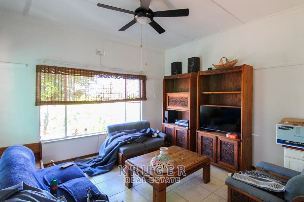 A living room featuring tiled flooring, a ceiling fan, and a large window providing natural light.