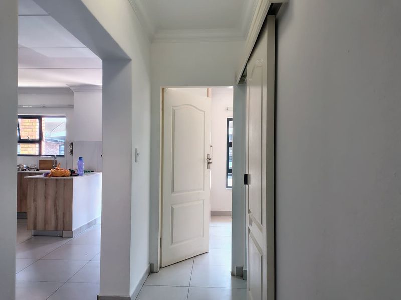 A bright, neutral hallway featuring tiled flooring, an archway leading to the kitchen, and a sliding door providing access to an adjacent room.