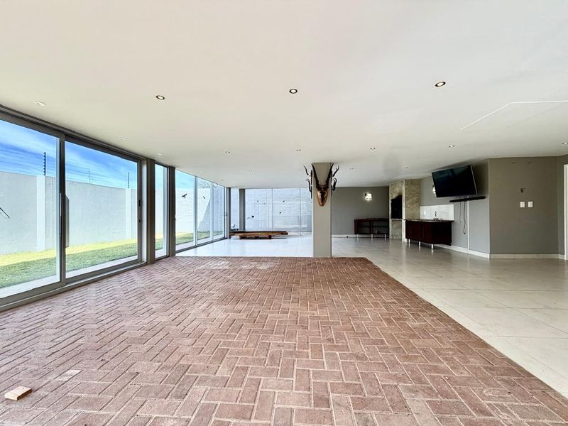 Spacious open-plan living area featuring a mix of brick and tile flooring, built-in bar, fireplace, and expansive sliding glass doors leading to the garden.