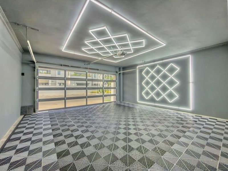 Modern, well-lit garage featuring custom LED ceiling and wall lighting, high-quality interlocking floor tiles, and a large sectional garage door.