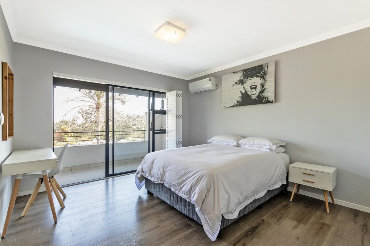 A bright bedroom featuring wood-look flooring, a wall-mounted air conditioning unit, and sliding glass doors that open onto a private balcony.