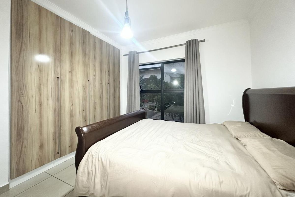 A well-maintained bedroom featuring floor-to-ceiling built-in wood-finish wardrobes, tiled flooring, and large windows with curtain tracks.