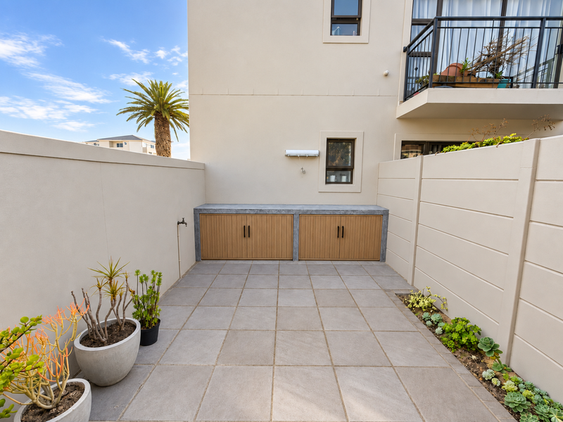 A well-maintained rear courtyard featuring tiled flooring, built-in storage cabinetry with a stone countertop, and a boundary wall with integrated garden beds.
