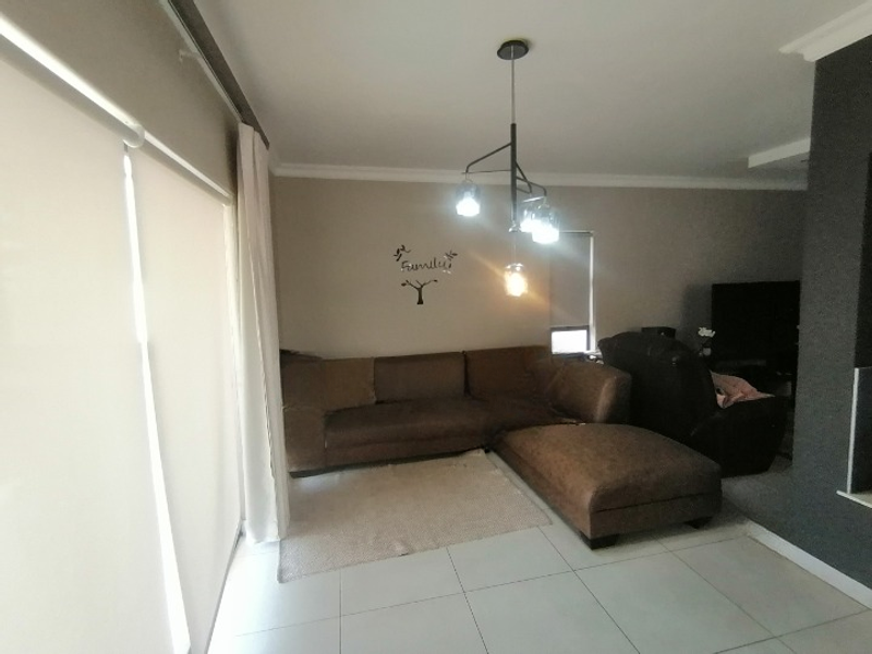 A comfortable living room featuring large format floor tiles, modern pendant lighting, and neutral wall finishes with roller blinds for privacy.