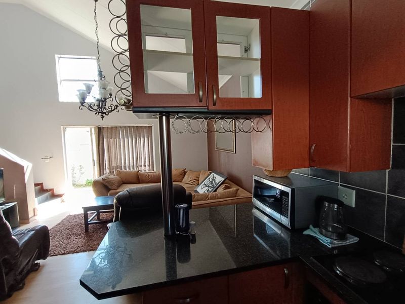 Open-plan kitchen featuring granite countertops and wood-finish cabinetry, overlooking a spacious living area with vaulted ceilings and natural light.