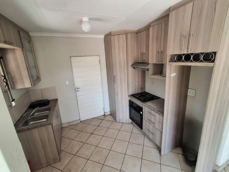 A functional kitchen featuring wood-look cabinetry, built-in oven and hob, stainless steel sink, and tiled flooring, offering a practical layout for daily use.
