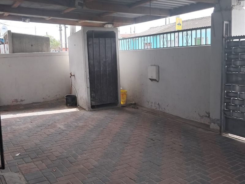 A covered outdoor parking area featuring paved flooring, a corrugated metal roof, and secure perimeter walling with a metal gate.