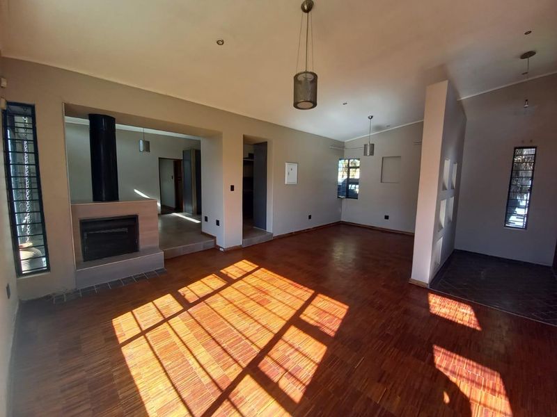 Spacious open-plan living area featuring warm parquet flooring, a central freestanding fireplace, and unique recessed wall niches, offering a bright and versatile layout.