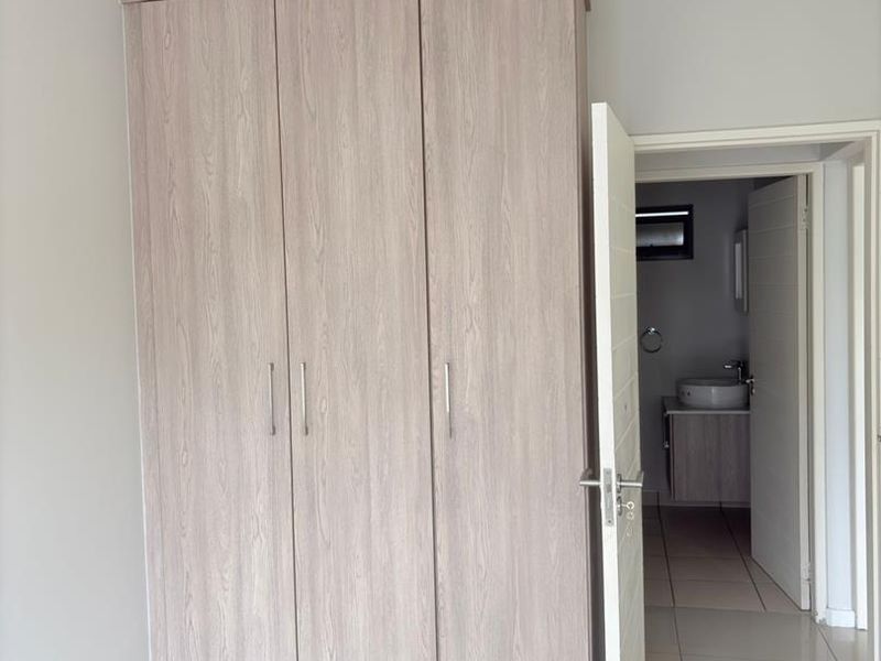 A clean bedroom featuring modern built-in cupboards, neutral tiled flooring, and direct access to an en-suite bathroom.