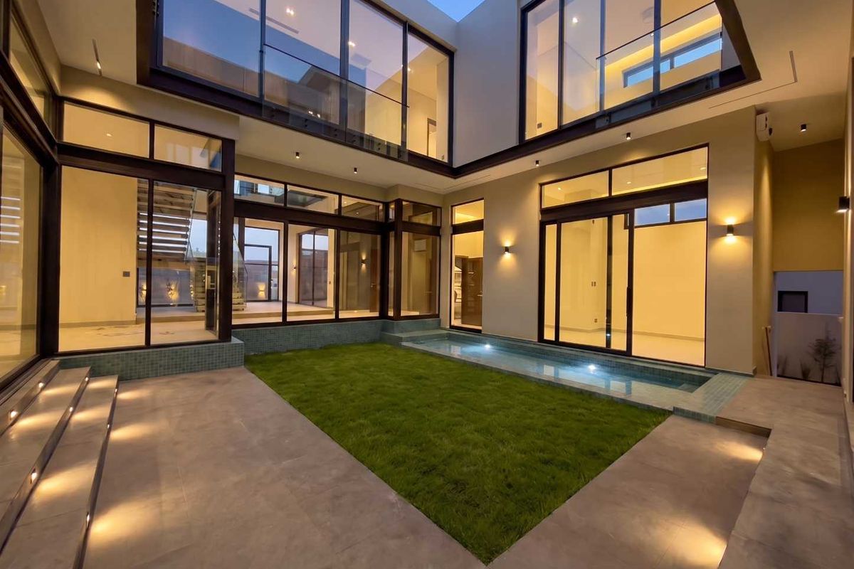 Modern courtyard featuring a private swimming pool, manicured lawn, tiled patio, and extensive floor-to-ceiling glass walls providing seamless indoor-outdoor flow.