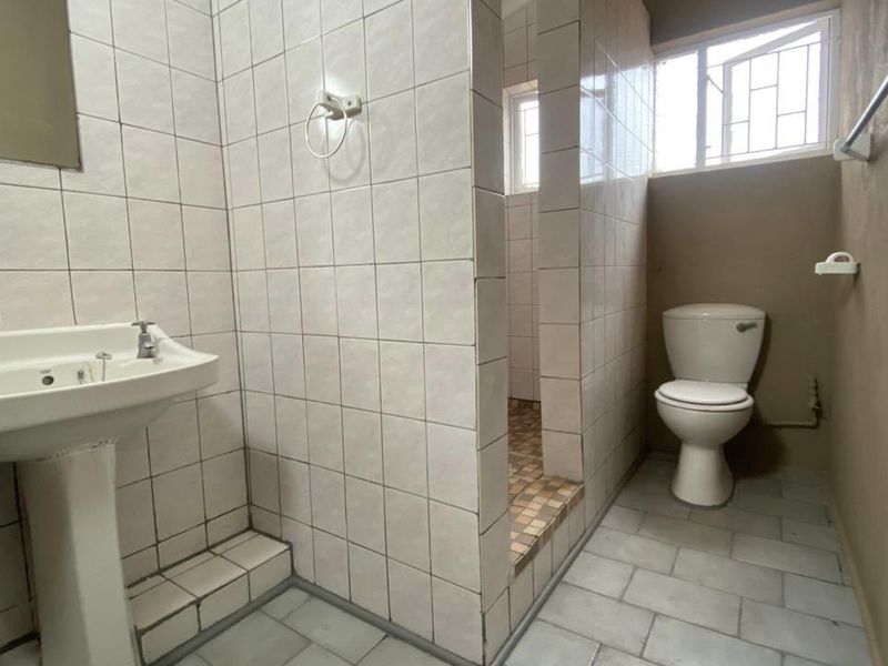 A functional bathroom featuring a pedestal basin, a tiled shower enclosure, and a toilet, with neutral wall finishes and tiled flooring.
