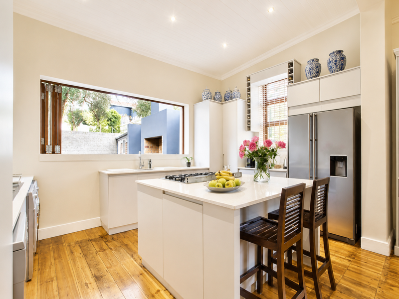 Modern kitchen featuring a central island with stone countertops, gas cooktop, ample built-in cabinetry, and warm timber flooring with a view to the garden.