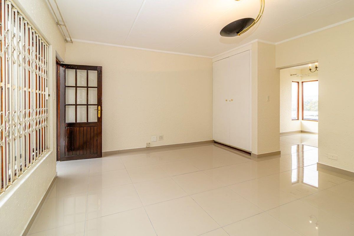 A bright, empty living area featuring neutral tiled flooring, a built-in cupboard, and a classic timber door with a security gate.
