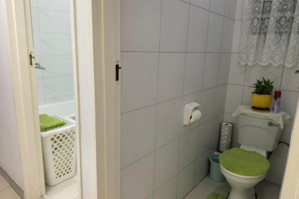 A functional bathroom featuring a standard toilet and tiled walls, with an adjacent view into a secondary bathroom area.
