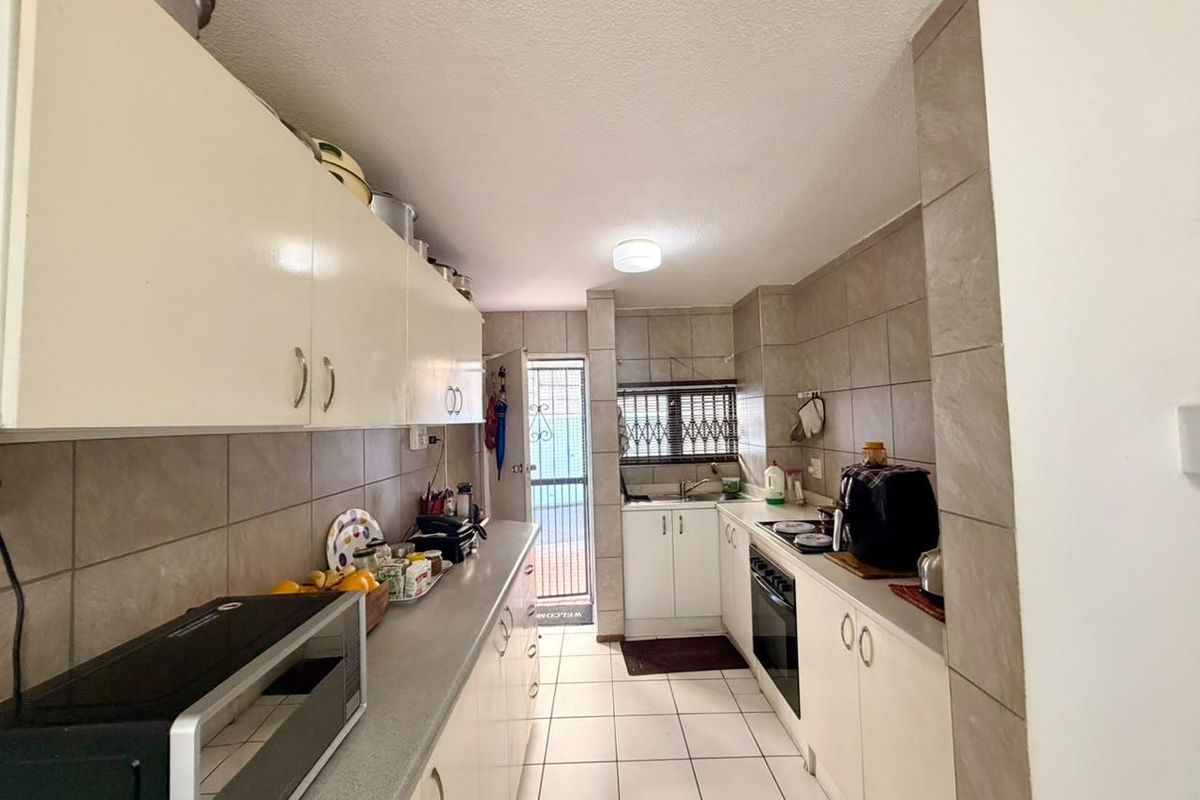 A functional galley-style kitchen featuring tiled walls and flooring, built-in cabinetry, a hob, and an oven, with direct access to an exterior area.