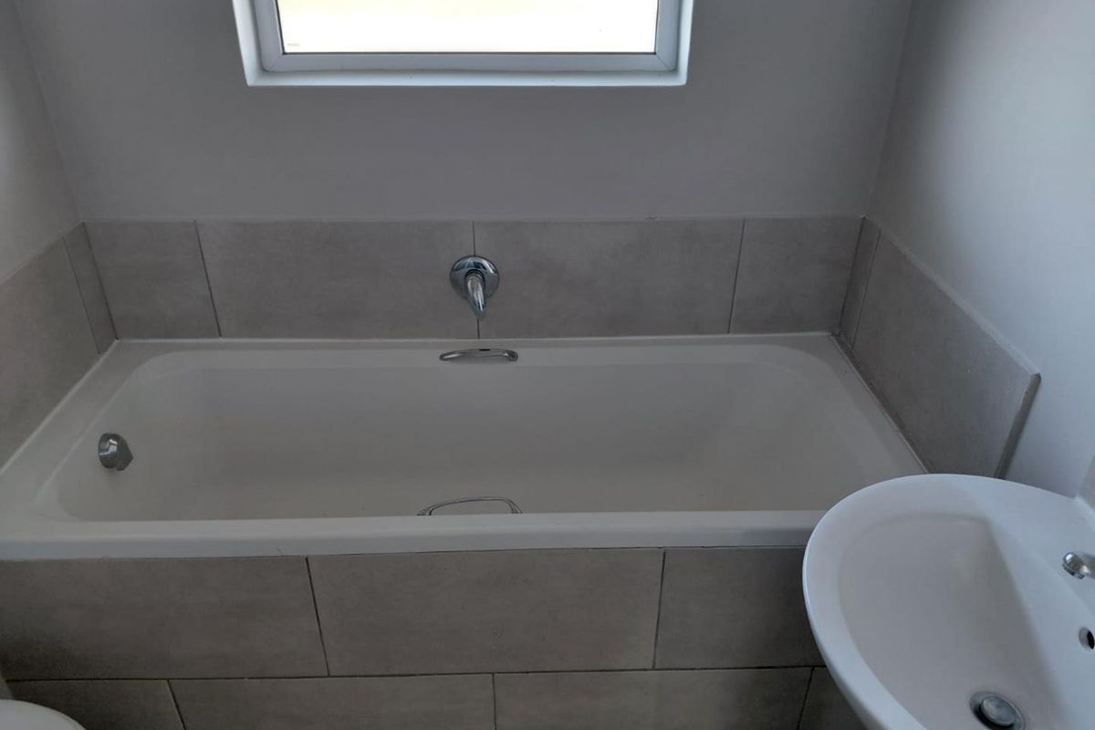 A clean, functional bathroom featuring a built-in bathtub with wall-mounted fixtures, neutral ceramic tiling, and a pedestal basin.
