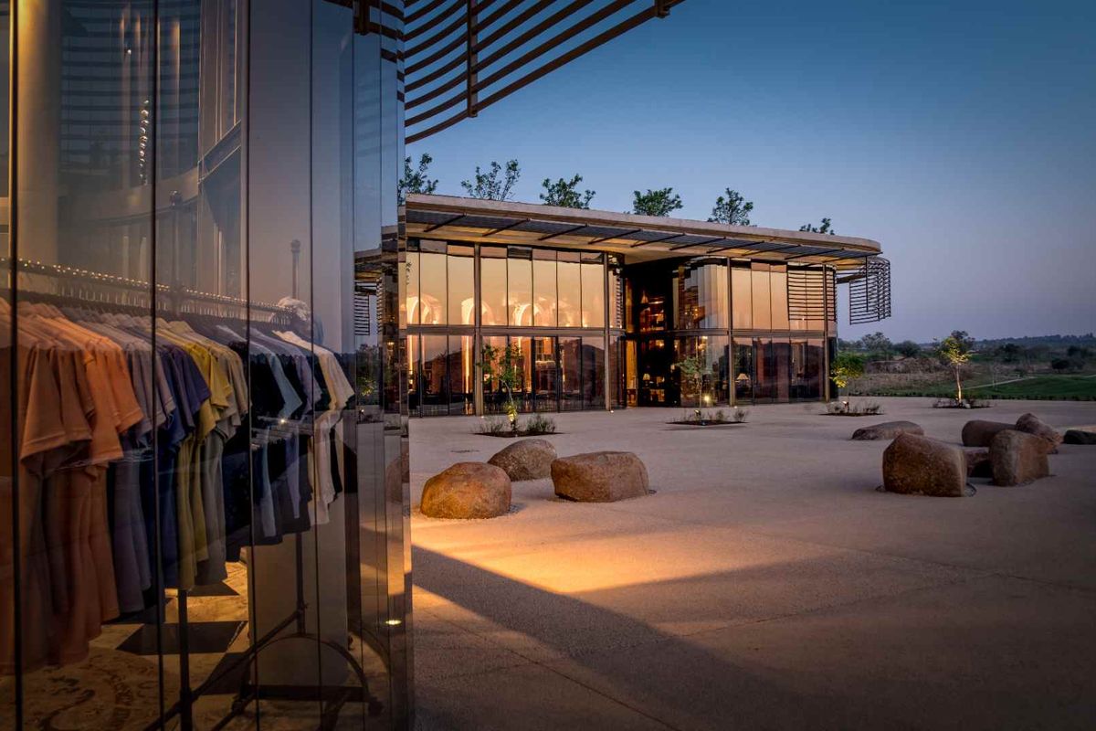 Modern architectural exterior featuring extensive glass curtain walls, concrete paving, and integrated landscape design at dusk.
